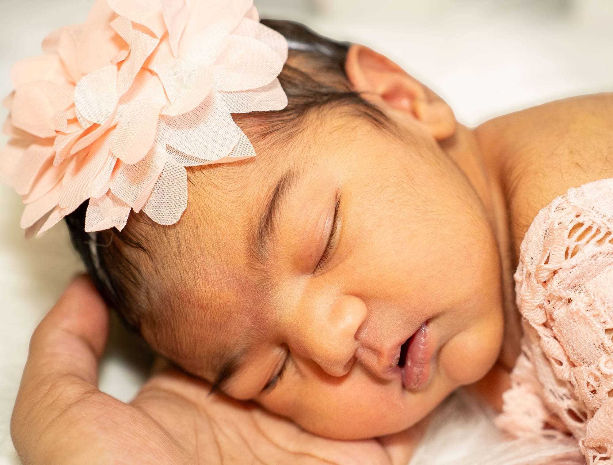 A newborn asleep with a large pink flower headband