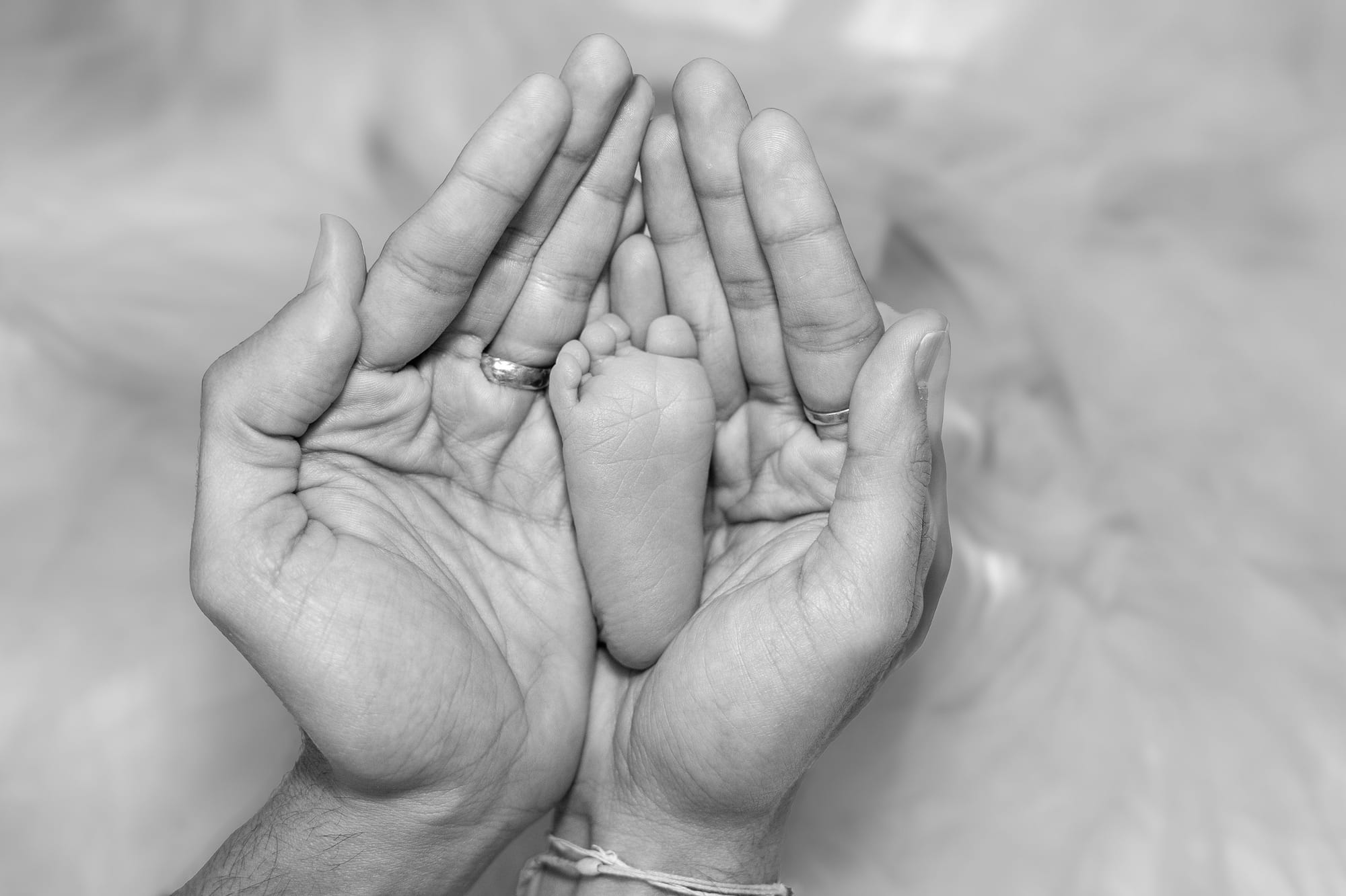 Tiny newborn feet held in mom's and dad's hands, in black and white