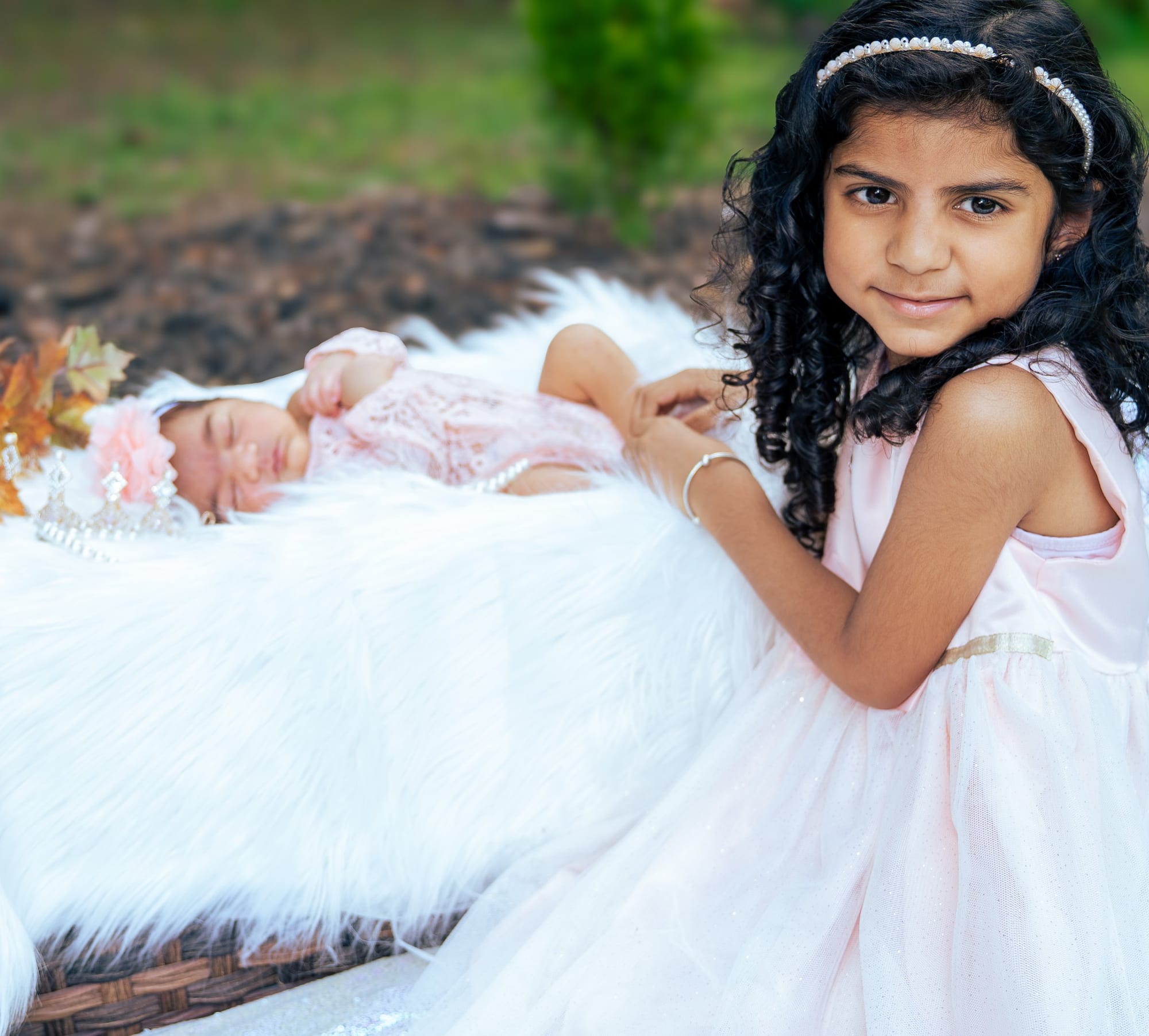 A big sister in a white dress sitting beside her sleeping baby sister